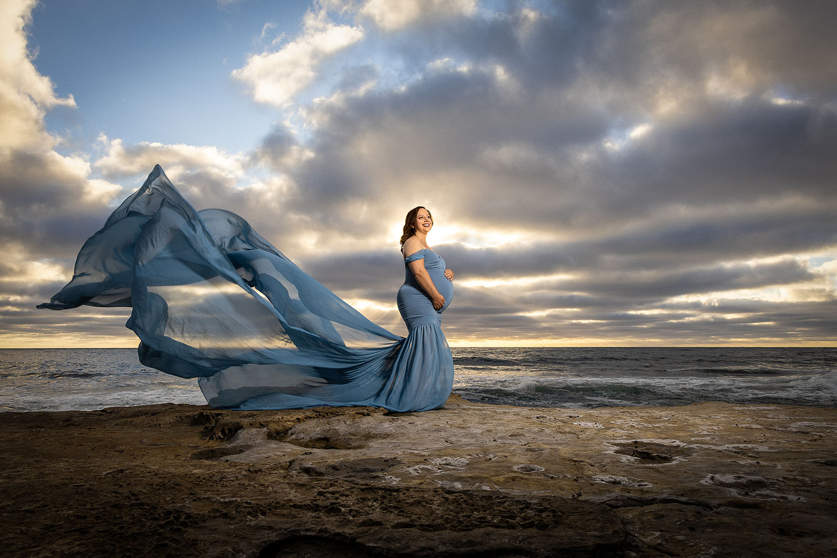 woman with pregnant belly at the coast with flowing maternity dress