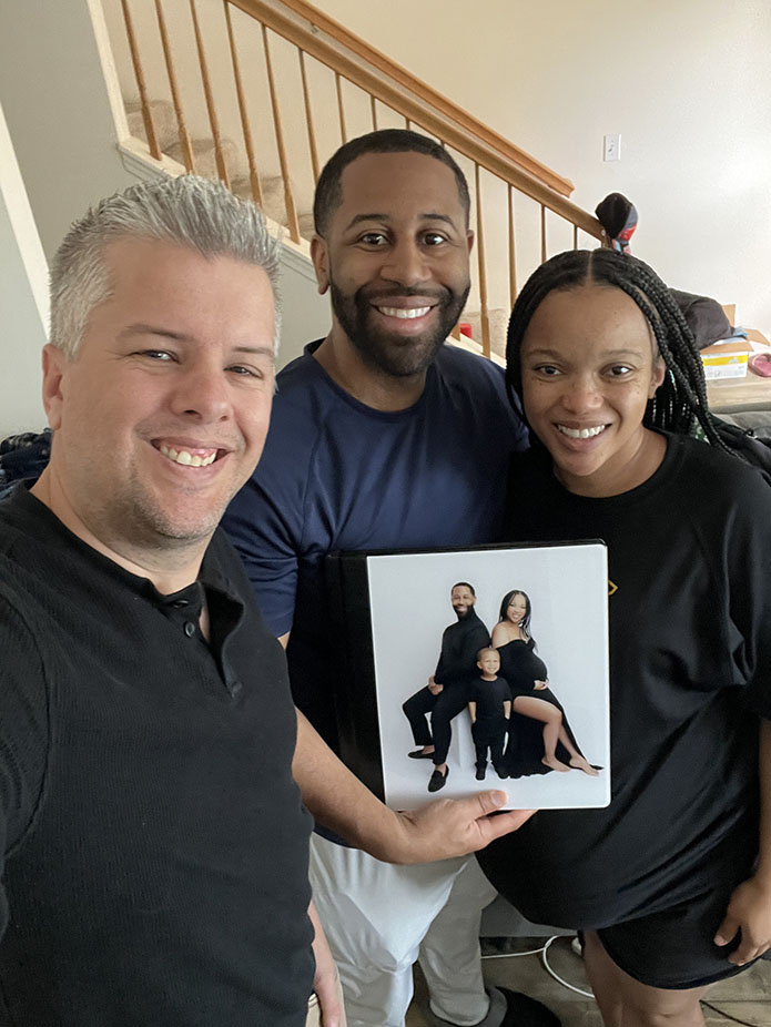 pro photographer poses with client couple holding their new maternity photo album