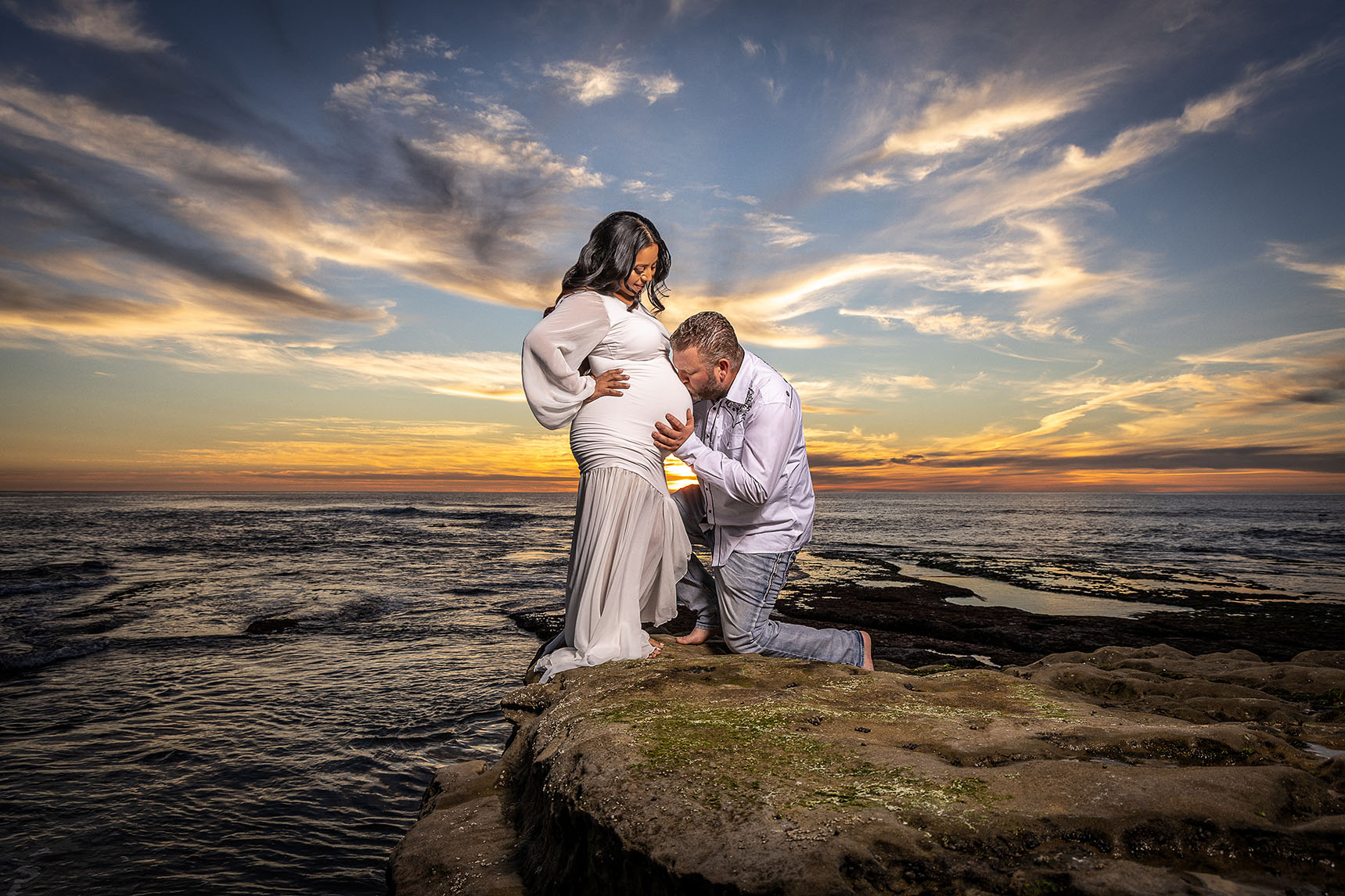 husband kissing pregnant belly pose with stunning sunset at La Jolla beach
